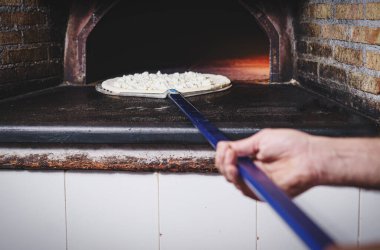 Pizza şefi beyaz bir pizza pişirir, sadece mozzarella, pizzacının taş fırınında, elinde kürek tutarken..