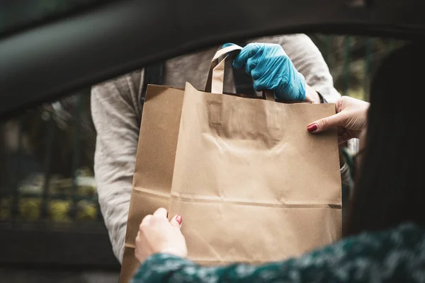 Woman hand receiving shopping brow paper bag out of car open window driving thru pickup from seller with blue glove - view from the car inside - room for text or copyspace