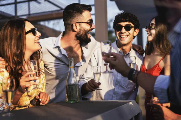 Best friends gathering at the outdoor sunset party carefree together talking, smiling and joking together drinking sparkling champagne - millenials group carefree at weekend standing on bar table