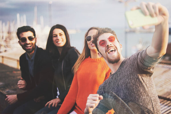 Best friends get-together outdoors sitting seaside and taking smartphone selfies - concept of friendship and happyness - filtered image
