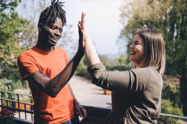 Afro-Afrikalı mutlu bir adamın gülümseyen ve beyaz bir kadınla beşlik çakışının profili. En iyi iki arkadaş el çırpıyor, parkta duruyor - arkadaşlık kavramı.