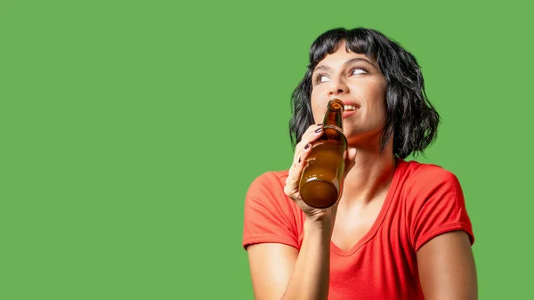 Portrait of a brunette woman holding a beer bottle and looking away from the camera, isolated on a green background - graphic resource with copy space for ad banners and web posters