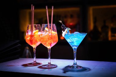 Three glasses with fresh alcohol drinks and with ice cubes on the bar counter of a night club - lifestyle concept