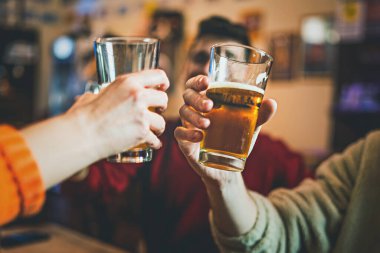 Happy friends having fun toasting beers in the pub - closeup shot shallow depth of field with focus on the hands - cropped image