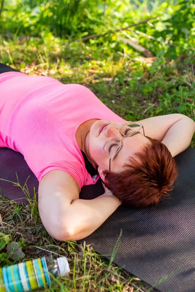 Yaz için forma girmeye çalışan güzel bir genç kadın. Parkta yoga minderiyle çalışıyor. 