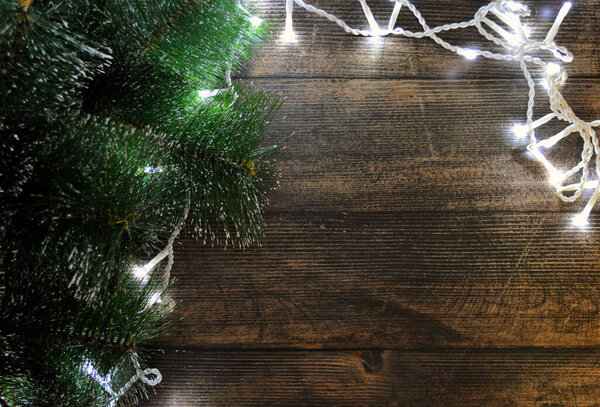 Christmas background of dark wood with fir branches and a garland. Copy space.