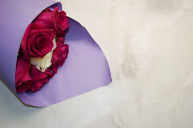 Mor ambalajlı kırmızı güller beyaz mermer arka planda yatıyor..