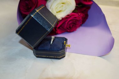 Mor pakette bir buket kırmızı gül ve beyaz mermer zemin üzerinde bir yüzük bulunan bir kutu. Evlilik teklifi kavramı