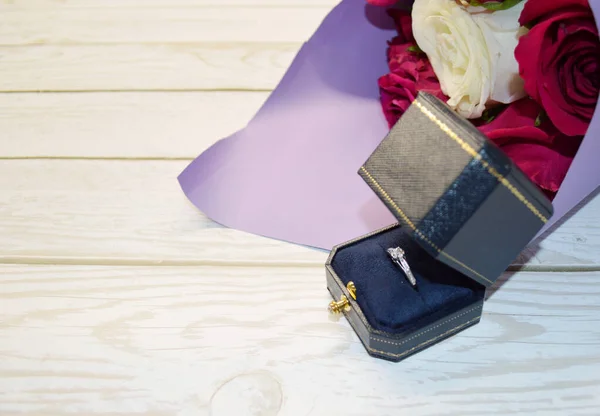 紫色包装中的一束红玫瑰和一个有戒指的盒子放在白色的木制背景上 婚姻建议的概念 — 图库照片