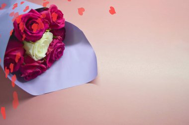 Mor ambalajlı kırmızı güller pembe arka planda yatıyor. Kalp şeklinde bokeh