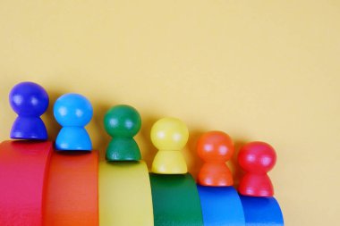 Sarı zemin üzerinde çok renkli merdivenlerde insanların ahşap taklidi. Montessori konsepti, otizm, çevresel oyuncaklar, azınlık seks kariyeri, sosyal merdiven, takvim, gökkuşağı partisi, LGBT topluluğu.