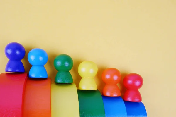 Sarı zemin üzerinde çok renkli merdivenlerde insanların ahşap taklidi. Montessori konsepti, otizm, çevresel oyuncaklar, azınlık seks kariyeri, sosyal merdiven, takvim, gökkuşağı partisi, LGBT topluluğu.