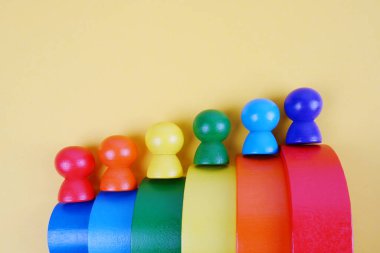 Sarı arka planda renkli merdivenlerdeki insanların ahşap taklidi. Montessori konsepti, otizm, çevre oyuncakları, azınlıkların cinsel kariyeri, sosyal merdiven, takvim, gökkuşağı partisi, LGBT topluluğu..