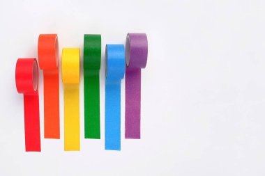 Beyaz bir zemin üzerinde çok renkli gökkuşağı renkli yapışkan bant ruloları. Yaratıcılık için parlak yapışkan dekoratif kurdeleler, hediye paketi, kırtasiye malzemesi satışı.