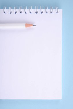 Mavi bir arkaplanda - bir çizim defteri veya defter, bir yay ve beyaz bir kalemle dikilmiş. Boş bir düzen yaratıcılık, çizim, yazım planları, notlar için bir alandır.