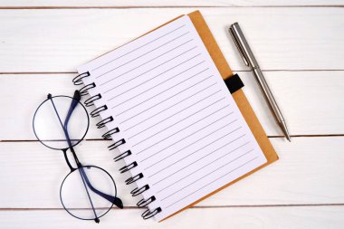 Not defteri, kalem, gözlük, beyaz tahta zemin. İş adamları, öğretmenler, sanatçılar için eşyalar. Not defterine yazma, yeni yılı planlama, yapılacaklar listesi.