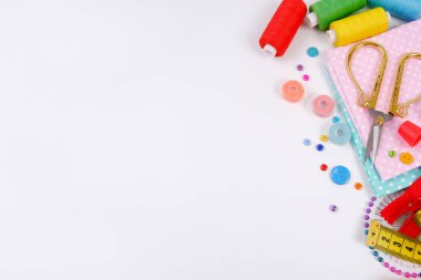 Dikiş ipliği, çok renkli düğmeler, makas, iğneler, yüksük, kumaş, fermuar gibi beyaz bir arka planda. El işi, giysi onarımı, nakış, dikiş aksesuarı konsepti.