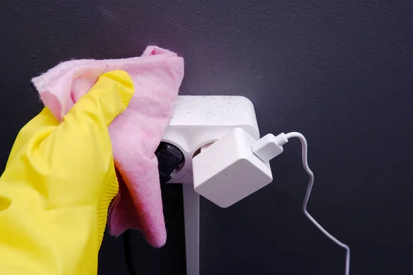 Sarı eldivenli bir kadının eli beyaz bir elektrik prizinden pembe bir bez ile tozu siler. Yakın görüş. Ev temizliği, temizlik şirketleri konsepti, insan sağlığına zarar veren tozlar.
