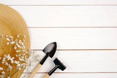 Beyaz ahşap bir arka planda saman bahçıvan şapkası, beyaz çiçekler ve bahçe aletleri olan bir kompozisyon. Çiftliğin tarihi. Hobi olarak bahçecilik, mevsimlik iş.