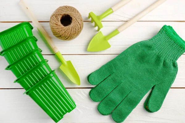 Garden supplies:shovels, rakes; green gardening gloves, green pots for seedlings, burning in a ball on a white wooden background.Gardening concept,spring sowing,transplanting of indoor plants