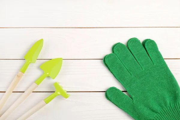 Garden supplies:shovels, rakes; green gardening gloves on a white wooden background.Gardening concept, spring sowing,transplanting of indoor plants.Copyspace