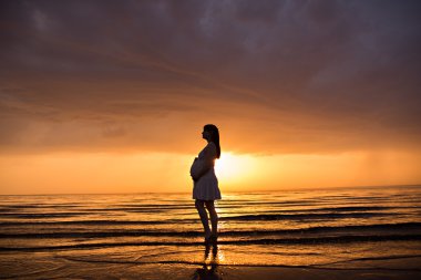 Deniz günbatımı, hamile bir kadın silueti