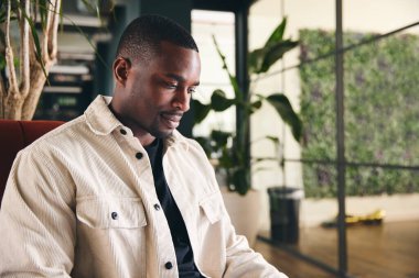 Modern açık plan ofisinde dizüstü bilgisayarla çalışan sıradan giyinmiş genç adamın yakın plan çekimi.