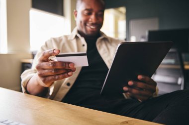 Smiling Man making online payment on tablet computer focused on credit card