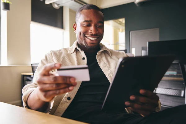 Smiling Man making online payment on tablet computer holding credit card