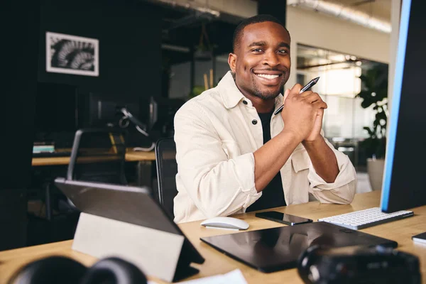 Young Black Male Advertising Marketing Or Design Creative In Modern Office Sitting At Desk Working On Computer Smiling to Camera