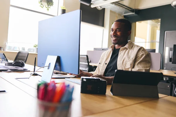 Young creative black man working on computer in modern office at desk smiling