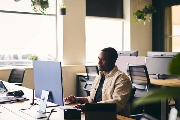 Young black man working on computer in modern office at desk wide with copy space
