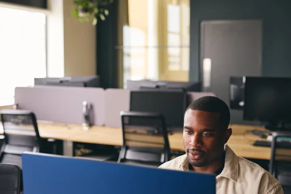 Young black man working on computer in modern office at desk smiling