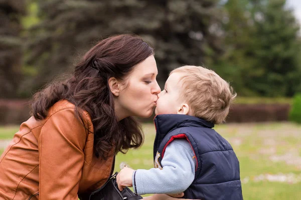 Glückliche Mutter spielt mit ihrem Sohn im Park, Sohn küsst seine Mutter — Stockfoto