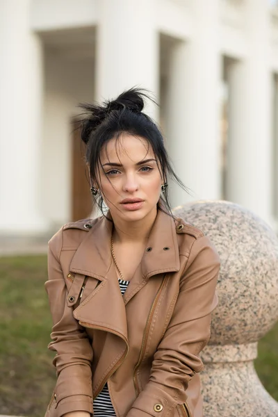 Menina sexy em vestido de couro sentado em um banco no parque . — Fotografia de Stock