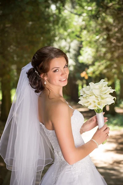 schöne Braut im Hochzeitskleid und Brautstrauss, freudig frisch verheirateten Frau mit Hochzeitsblumen, Frau mit Hochzeit Make-up und Frisur. wunderschöne junge Braut im Freien. Braut Bräutigam warten. Braut