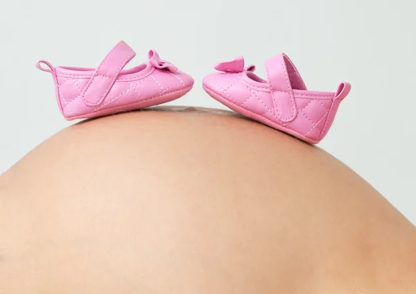 Foto de una mujer atractiva que está embarazada de 38 semanas sosteniendo botines de bebé rosados y blancos en su barriga . — Foto de Stock