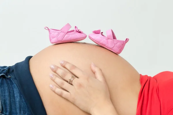Фото привабливої жінки, яка 38 тижнів вагітна, тримаючи рожеві та білі дитячі пінетки на животі . — стокове фото