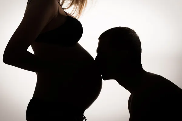 Silhouette profile of a man kissing pregnant belly of his woman.Family, love and care concept. — Stock Photo, Image