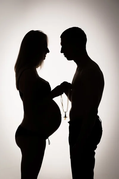 Silhouette profile of a man kissing pregnant belly of his woman.Family, love and care concept. — Stock Photo, Image