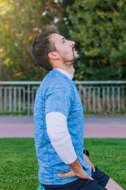 Atletik yorgun bir gencin dikey görüntüsü koşu pistinde uzanıyor gökyüzüne bakıyor ve eğitimden sonra soluklanıyor..