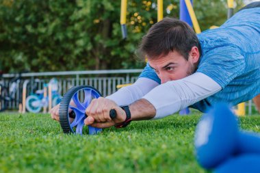 Genç ve güçlü bir sporcu, karın kaslarını doğal park yerinde tekerlekle çalıştırıyor..