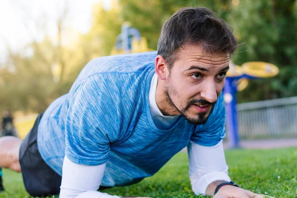 Sporcu, kişisel antrenörüyle birlikte açık hava antrenmanı sırasında karın tahtası egzersizi yapıyor..