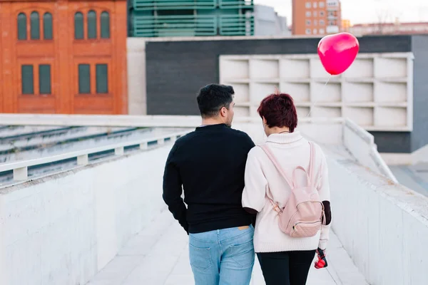 2人の若いカップルが街を後方に歩き バレンタインデーに赤いハート型の風船を抱いています 恋人と初恋の概念 — ストック写真