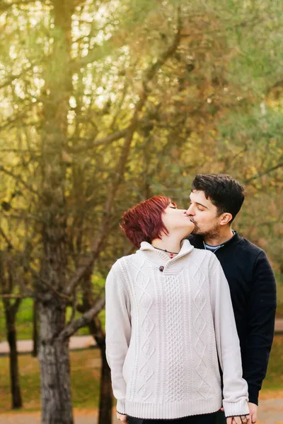 森の中でキスして抱きかかえる二人の若者の垂直イメージ 背景にはかなさの木と晴れた秋の日 — ストック写真