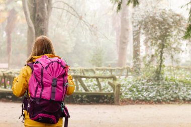 An adventurous female hiker, walking through the mountains in nature on a rainy day, wearing a yellow raincoat and a backpack with all the survival gear. Huge copy space on the right.