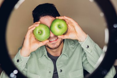 Genç bir online girişimcinin beslenme vlog 'u. İnternet sitesi için video kaydederken gözlerinde iki yeşil elma olan beslenme uzmanı bir adamın komik yüzü..