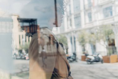 Durakta otobüs bekleyen genç bir kadının camdan yan görüntüsü..