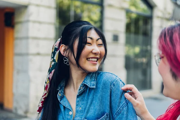 Optymistyczna Młoda Japonka Dżinsowej Koszuli Uśmiechnięta Patrząca Najlepszą Przyjaciółkę Podczas — Zdjęcie stockowe