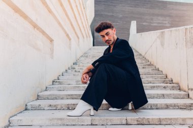 Yüzünde beyaz topuklu ayakkabılar olan, şehirde merdivenlerde çömelmiş kameraya bakan kadın erkek vücudu.